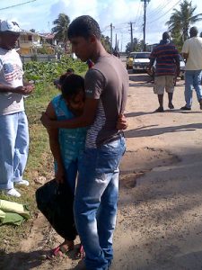 Kevin Rambissoon comforts his mother as she arrives to find the lifeless body of her husband at the roadside