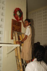 A student places the wreath above the plaque which has the names of the fallen soldiers from Queen’s College 