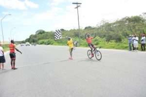 Hamzah Eastman raises his hands in triumph after winning the first stage of the Dr Cheddi Jagan Memorial three-stage cycle road race on the West Demerara yesterday, as his teammate and winner of the veterans’ category Junior Niles (left) looks on. (Samuel Maughn photo)