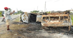 Pastor Narine Khublall taking a photograph of some of the burnt-out vehicles outside of his home yesterday   