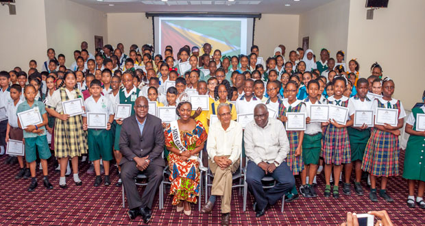 ‘CONGRATULATIONS!’ In photo, from left, are Chief Education Officer Mr Olato Sam along with Miss Guyana United Kingdom, Zena Bland; Minister of Education Dr Rupert Roopnaraine; and chairperson of the ceremony ACEO [Primary) Mr Marcel Hutson, posing with the Top 1% students who excelled at the recent NGSA exams (Delano Williams photo)