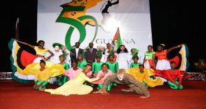 Performers along with Minister Henry and the logo winners on stage, with logo in background 