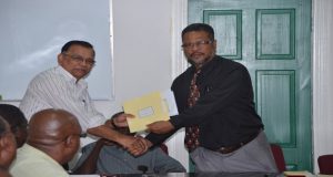 Chief Labour Officer Charles Ogle presents the new wages and salaries agreement to GPL Human Resource Director  Bal Persaud  
