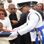 Assistant Commissioner David Ramnarine presents a flag of the Guyana Police Force to the wife and youngest son of ACP Balram Persaud [Samuel Maughn photo)