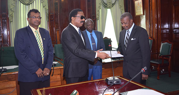 Attorney General and Minister of Legal Affairs Basil Williams hands over the Commission of Inquiry report into the death of Dr Walter Rodney to Speaker of the National Assembly Dr Barton Scotland on Wednesday in the Parliament Chamber. Also in photo are Minister of Public Security Khemraj Ramjattan [left) and Clerk of the National Assembly ,Sherlock Isaacs (centre)