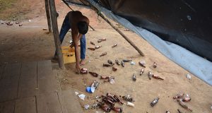A man picks up scattered beer bottles from around a “kaimoo” along the Amaila Falls road in the Kuribrong Mining District, Region Eight