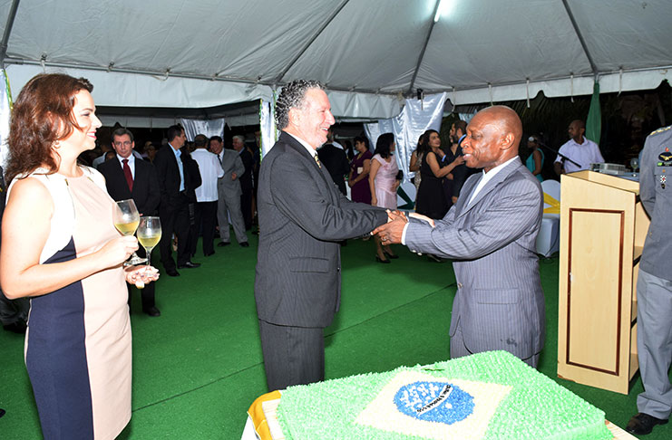 Ambassador Lineu de Pupo Paula and Minister Carl Greenidge exchange a firm handshake as they are about to cut the anniversary cake
