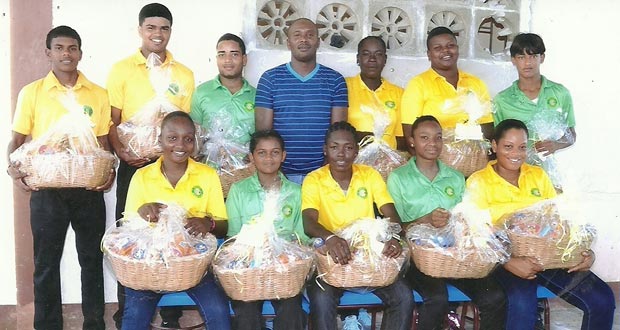 Eleven members of the Rose Hall Town Youth and Sports Club proudly display their hampers received, after being honored for their national selection during the year. Sitting at centre is West Indies second female centurion Shemaine Campbelle.