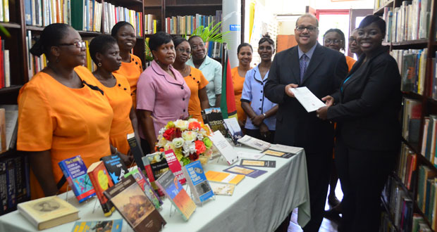 Mr Siefy Shahabuddeen handing over the donation of books to acting Deputy Chief Librarian,  Nadine Moore, while other staff members look on.