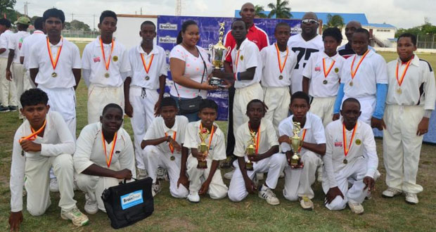 Yes we did it! The victorious Transport Sports Club Under-15 team strikes a pose with their spoils, even as their skipper Colin Barlow receives the GCA/BrainStreet Under-15 Cup from Mrs. Adrienne Harmon. (Photo by Adrian Narine)
