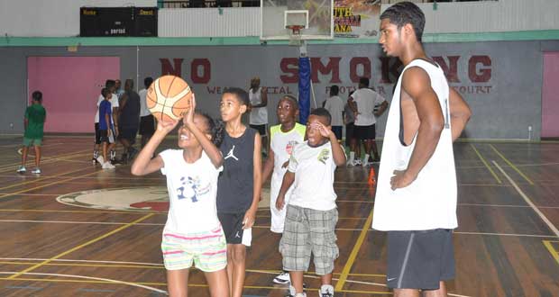 National point guard Akeem Kanhai looks on as a YBG camp participant tries to execute what she was taught (Delano Williams photo)