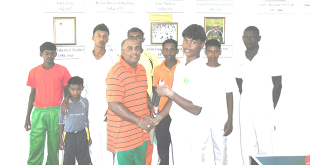 Former national leg spinner Arjune Nandu (left) proudly presents one of the bats to Vivekanand Jagjit of PMCC in front of the club’s Wall of Fame, while his teammates look on proudly in the back ground. (Calvin Roberts)