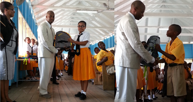 President of the Brickdam Secondary Alumni Association (NY Chapter) Mr Winston James hands over backpacks to students.