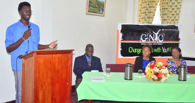 Board Trustee, Jamal Goodluck at the podium, with head table from left, CUSO volunteer, Rhikkie Alexander, and Board Trustees Tiffany Daniels and Andrea Bryan-Garner