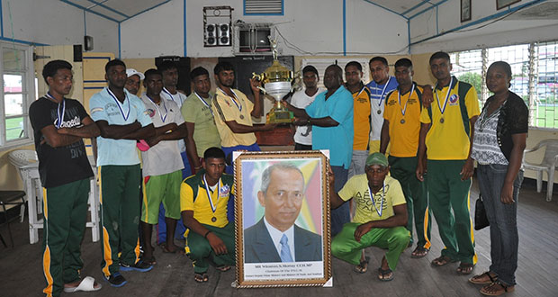 Former MP and General Secretary of PNC/R Aubrey Norton (right) presents the trophy to captain of the victorious Regal XI team Mohamed Ayube, in the presence of other members, who strikes a pose with a portrait of the late Winston Murray.