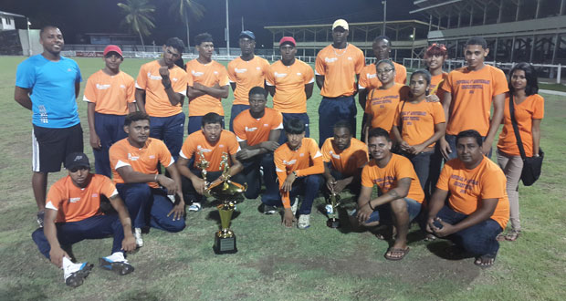We are still the champions! The victorious orange clad Universal DVD Berbice Titans strikes a pose with their spoils and Chief Executive Officer of Universal Solutions and Universal DVD Store Vicram Seubarran (stooping at right). Coach Julian Moore is at left (blue jersey).