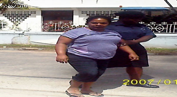 The teenager's mother, Kulwantie DeSouza, called “Deena,” being escorted by a police rank outside the Central Police Station in New Amsterdam