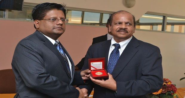 Finance Minister Dr. Ashni Singh receives a copy of the commemorative coin from Bank of Guyana Governor Dr Gobind Ganga