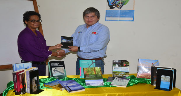 Marco Camacho, representative of the GSJV Aurora Project, hands over the books to Dr Elizabeth Ramlal, UG Deputy Vice Chancellor, Planning and Development