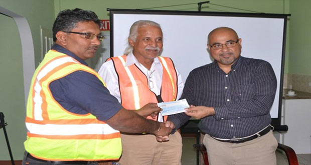 Co-Chairman of CGX Energy Inc., Professor Suresh Narine handing over the cheque to Gaico Construction Inc., Managing Director, Komal Singh in the presence of the Ministry of Public Infrastructure’s Technical Advisor, Walter Willis at the CGX New Market Street Office yesterday