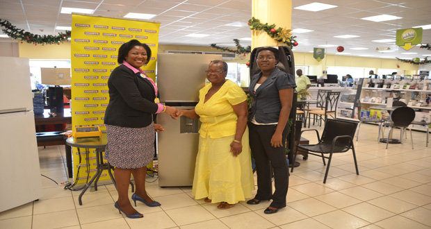 General Manager of Courts Main Street Branch Sharon Persaud formally hands over the Samsung inverter fridge to pensioner Dolores Daniels in the presence of Head of GEA Energy Statistics Division Shevon Wood.