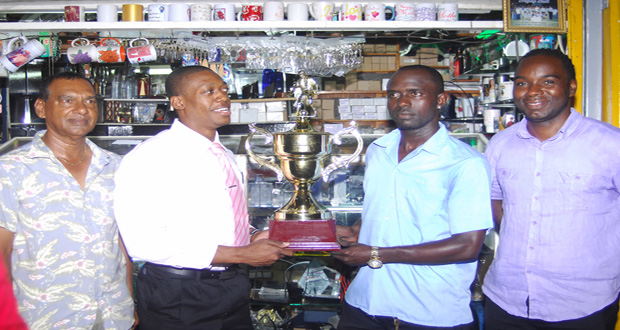 Captains of tonight's FUTSAL final holding the Trophy Stall sponsored winners' trophy; at left is Kerwin Clarke of the Ministry of Foreign Affairs and at right, Phillip Rowley of Banks DIH. At extreme left is Ramesh Sunich Managing Director of Trophy Stall, and far right is Tournament Organiser Esaun Griffith