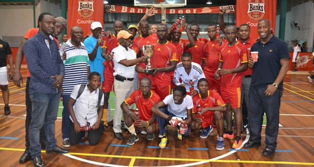Winning Captain Phillip Rowley collecting the winners' trophy  from Minister of Foreign Affairs and first Vice-president Carl Greenidge surrounded by team mates and officials  of Champions Banks DIH.