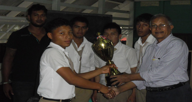 The victorious Skeldon High School receive the trophy from organiser Mr Krishnanand Raghunandan . Their coach Joseph Brijbilas looks on.