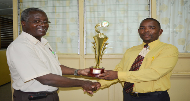 GNNL Personnel Relations Manager Colin Alfred presenting the trophy to an official of the Regional Science, Mathematics and Technology Fair, set for March