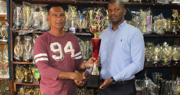 Trophy Stall Managing Director  Ramesh Sunich hands over one of the trophies up for grabs to GTTA president Godfrey Munroe.