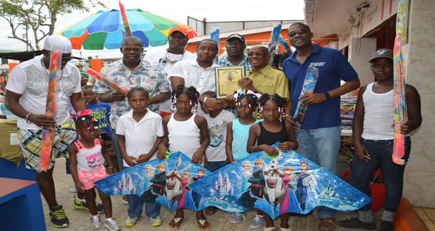 The businessmen pose with Minister of Public Infrastructure, David Patterson, and former City Mayor Hamilton Green (second and third right respectively) as they share a moment with children who were feted