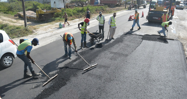 Workmen level asphalt placed on the road as part of the quality testing process