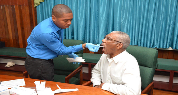 President David Granger allows the painless removal of the sample for his Ancestry DNA test by Mr. Shawn Manbodh, Quality Manager and Medical Technologist at Eureka Labs. This was done at State House on Monday (Ministry of the Presidency photo)
