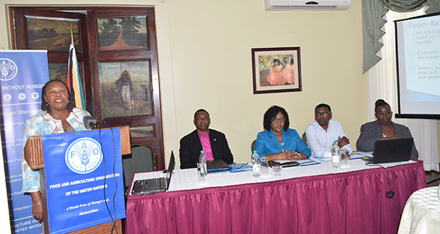 Dr Pauline Samuda, FAO Regional Consultant, addressing the gathering.  Seated, from left, are:  FAO Representative Reuben Robertson; Minister within the Ministry of Public Health, Dr Karen Cummings; Chief Medical Officer, Dr Shamdeo Persaud; and Ninian Blair, Director (Ag), Food Policy Division