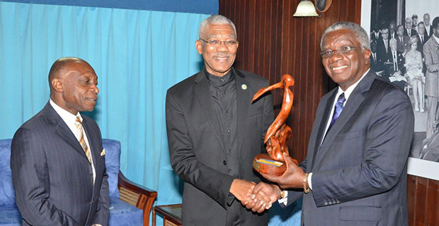 Prime Minister Freundel Stuart presents a gift to President David Granger for the people of Guyana, during a meeting at the Ministry of the Presidency. Foreign Affairs Minister Carl Greenidge looks on. (Ministry of the Presidency photo)