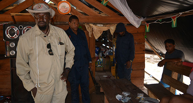 Senior Mines Officer of the GGMC Josiah stands in a “kaimoo” in the Kuribrong Mining District with police ranks as they searched and conducted investigations