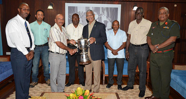 President David Granger is presented with the championship trophy by the GuyanaNRA's captain, Mr Mahendra Persaud, while members (from L-R) Mr Ryan Sampson, Mr Dylan Fields, Mr Lennox Braithwaite, Mr Terrence Stuart, Mr Paul Slowe and Brigadier General Mark Phillips look on.