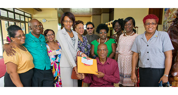 Henry Rodney (Seated) receives the money raised from the 'Rukatuks' Benefit Concert along with other donations from Sheron Cadogan- Taylor and is surrounded by fellow artistes and wife (second right).