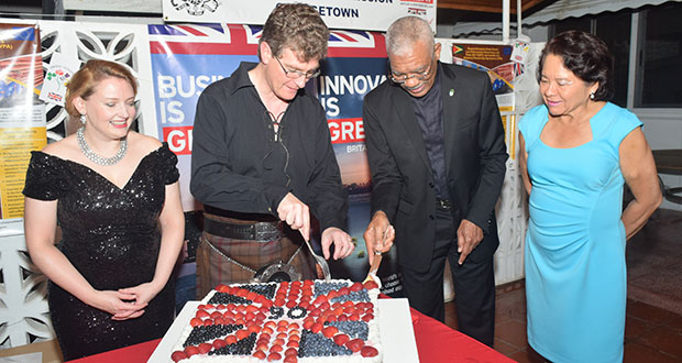 President David Granger and British High Commissioner Greg Quinn cutting a cake in honor of Her Majesty, Queen Elizabeth 11 90th birthday. Their wives, The First Lady Sandra Granger and Wendy Quinn look on with a sense of pride