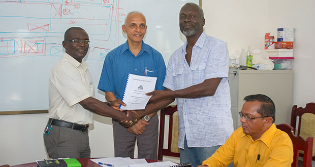 Permanent Secretary in the Ministry of Communities Emil McGarrell handing over the contract to Samuel Wright in the presence of Minister of Communities, Ronald Bulkan.