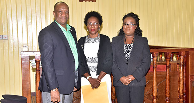 Retired Colonel Windee Algernon stands between Minister of State Joseph Harmon (right) and Magistrate Fabayo Azore (left) on Friday at the Georgetown Magistrates’ Court