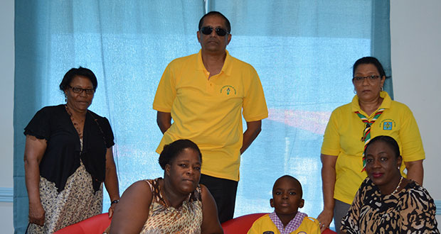 Eight-year-old Nick Omari Joseph (seated at centre) awaits his flight at the Eugene F. Correia International Airport, Ogle. Also in the photograph are his mother, Delia Finistere (seated left); Minister within the Ministry of Education, Nicolette Henry; and representatives of the Scouts Association of Guyana, including its President, Ramsay Ali (standing at centre)