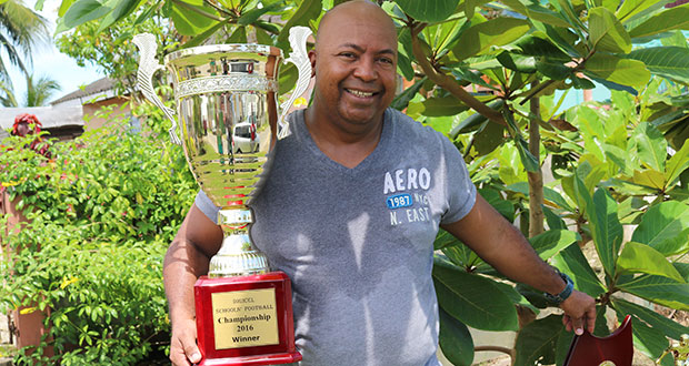 A smiling Director/Principal of Chase Academy, Henry Chase, poses with Digicel's 2016 Championship trophies for photographer Lorraine Harris.
