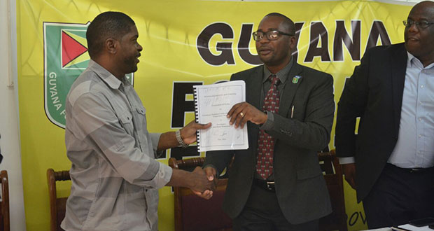 Contractor Dwain Ferdinand collects the inked contract from GFF president Wayne Forde as FIFA development officer Howard McIntosh looks on.