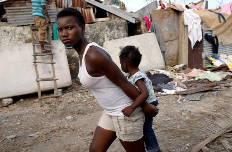 A woman carries a child as they walk in front of destroyed houses after Hurricane Matthew had passed Jeremie, Haiti, October 7, 2016.REUTERS/Carlos Garcia Rawlins