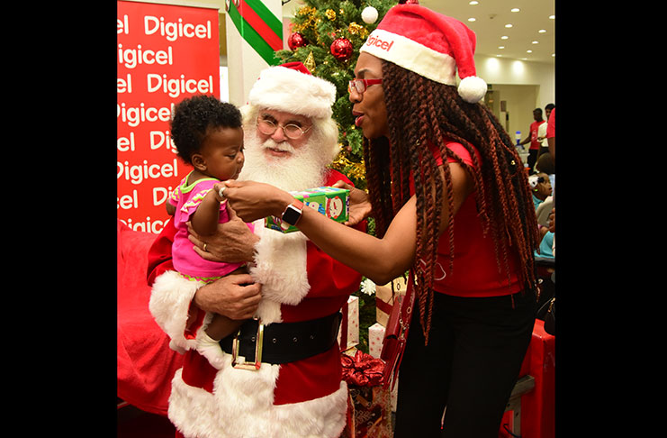 Cellular phone giant Digicel on Thursday launched its #GetGifted Christmas promotion at the Giftland Mall,
Turkeyen, Greater Georgetown. In this Adrian Narine photo, Digicel’s Marketing Manager Jacqueline James
interacts with a baby in the company of Santa Claus.