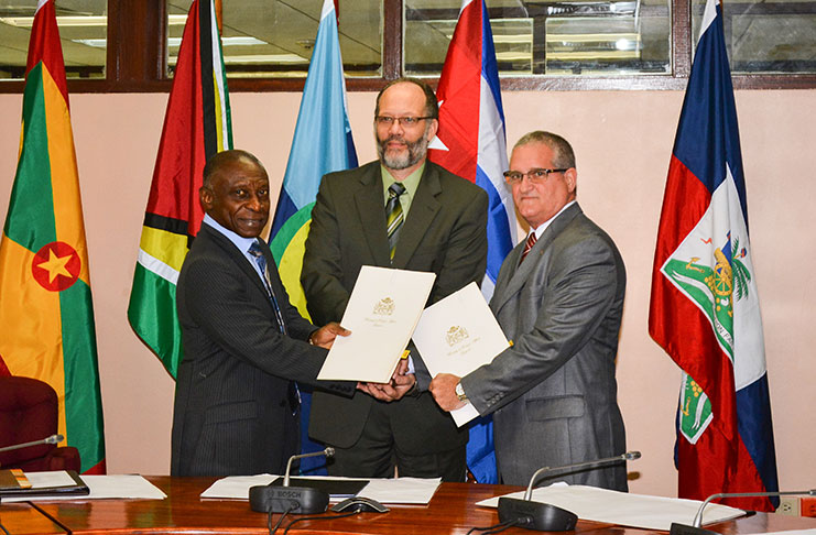 Foreign Affairs Minister Carl Greenidge, CARICOM Secretary-General Irwin LaRocque and Cuban Ambassador Julio Cesar Gonzalez Marchante sharing hands as they hold copies of the tripartite agreement
(Photo by Samuel Maughn)