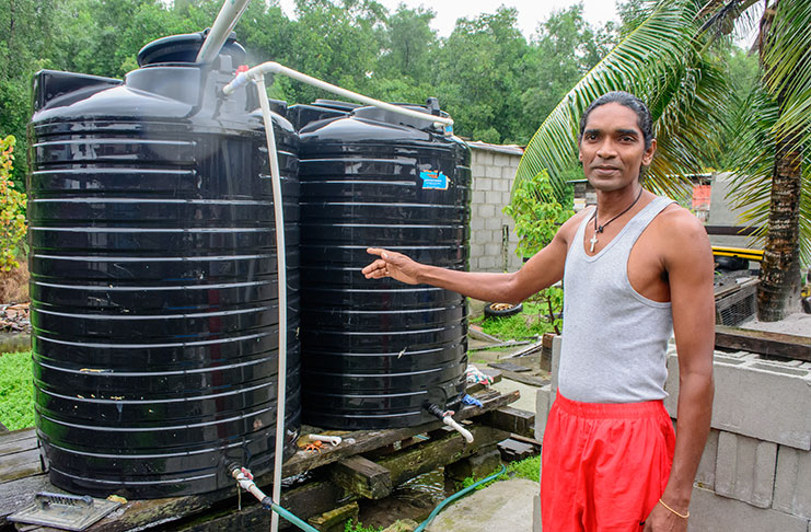 Sunil Dat pointing to one of his black tanks that collects rainwater for consumption during the rainy season