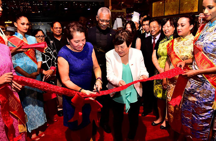 First Lady Sandra Granger, assisted by New Thriving Restaurant co-proprietor Che Jian Ping, cuts the ceremonial ribbon in the presence of staff and President David Granger to open the new restaurant