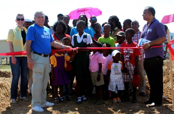 A school child with help from Food For the Poor officials, cut the ceremonial ribbon to open the New Hope Community Development Project